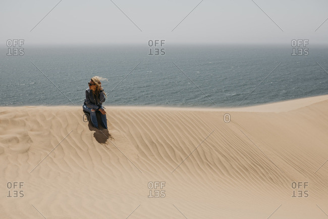 Namibia- Walvis Bay- Namib-Naukluft National Park- Sandwich Harbour- woman sitting in dune landscape at the sea