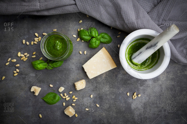 Glass of homemade pesto Genovese- mortar and ingredients on grey ground