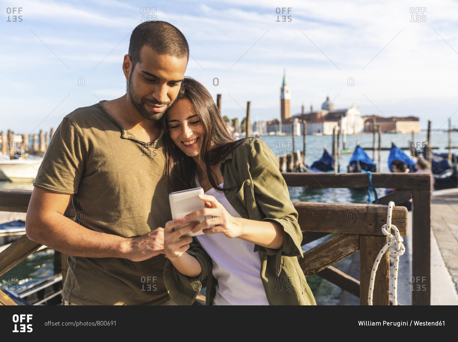 Italy- Venice- affectionate young couple with cell phone and gondola boats in background