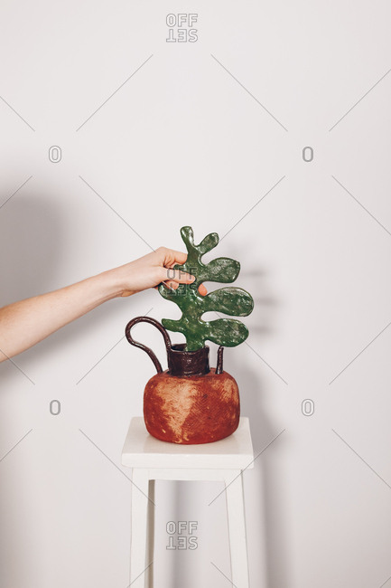 Female ceramist arranging a self-made ceramic bowl in front of a white wall background. Authentic vase and flowerpot artwork.
