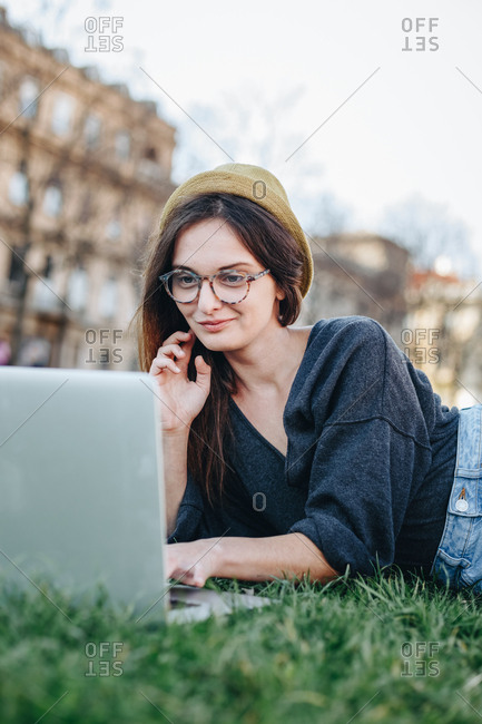 Authentic portrait of happy young freelancer woman sitting in park and using laptop to surf the internet and check for job opportunities.