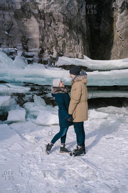 A young couple of lovers look at each other on a journey, standing in front of the ice cave
