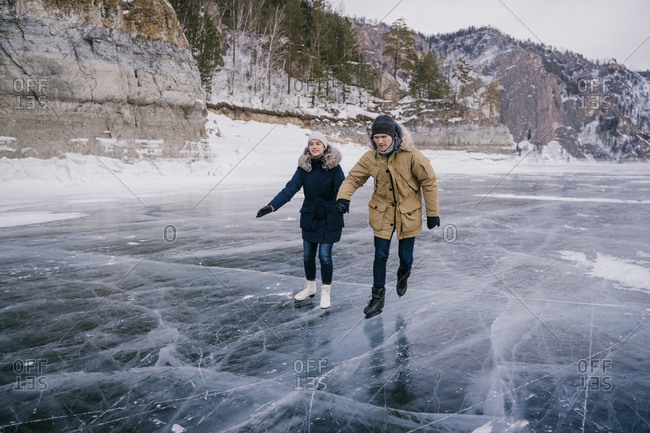 A man and a woman go ice-skating on the ice of a frozen lake and look ahead.