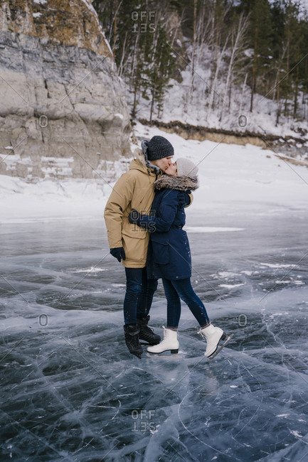 Man and woman kiss, skating on the ice of a frozen lake and look ahead.