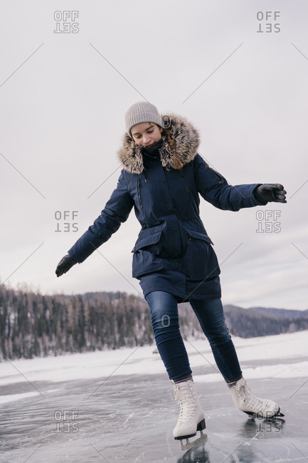 Young beautiful woman skates on the ice of a frozen lake in winter.
