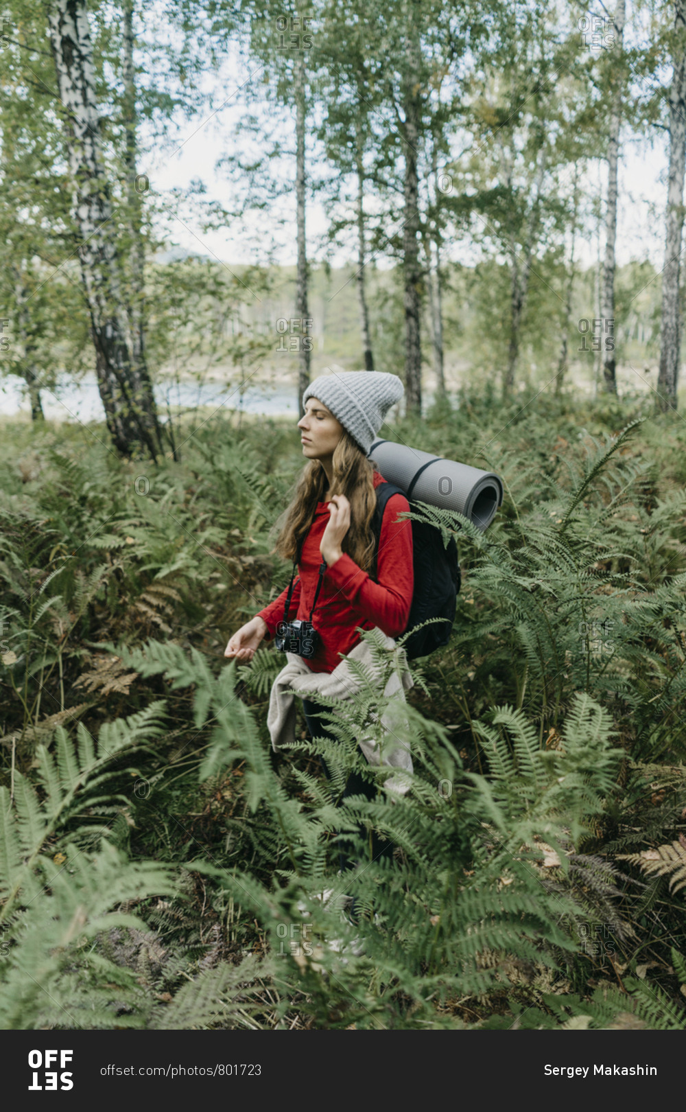 Portrait of a beautiful young woman with backpack and film camera takes photos in the fern bushes in the forest