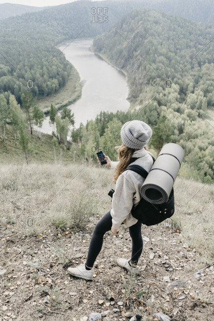 Beautiful young woman with backpack and film camera takes pictures on her phone.
