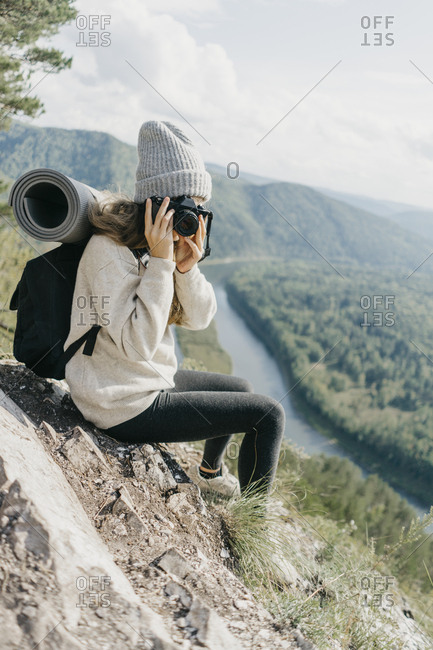 Portrait beautiful young woman with backpack and film camera sits on a mountain with an incredible view.