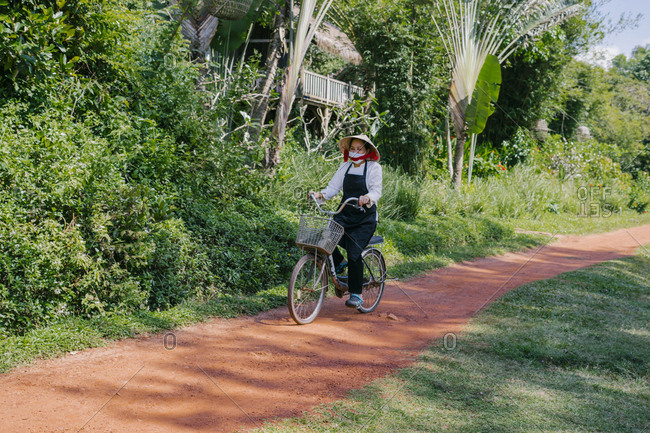 Phu Quoc, Vietnam - January 18, 2019: Vietnamese woman in a hat riding a bike with a basket to work at the hotel.