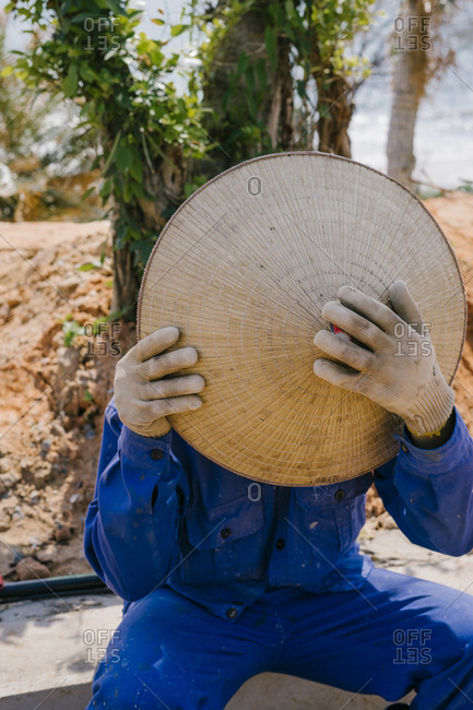 Vietnamese Builder covers his face with a straw hat.
