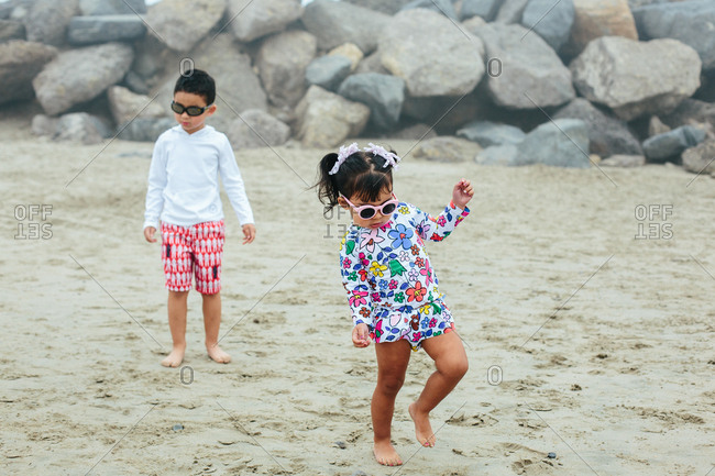 Toddler Girl Walks on Sand and Wears Sunglasses At Beach
