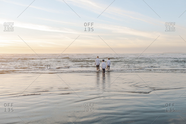 Rear view of kids far away standing in the waves during sunset
