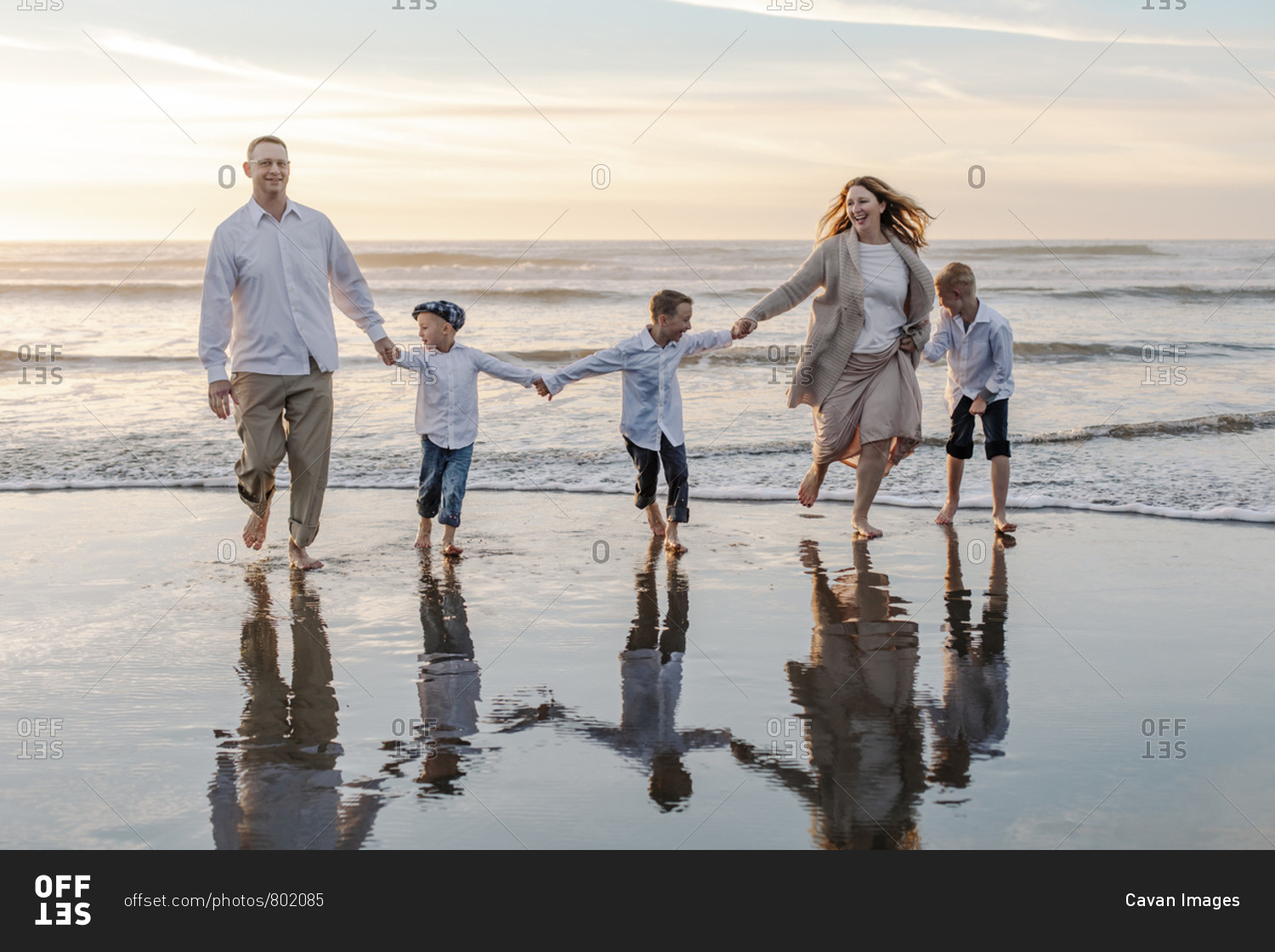 Happy family holding hands against sky during sunset at beach