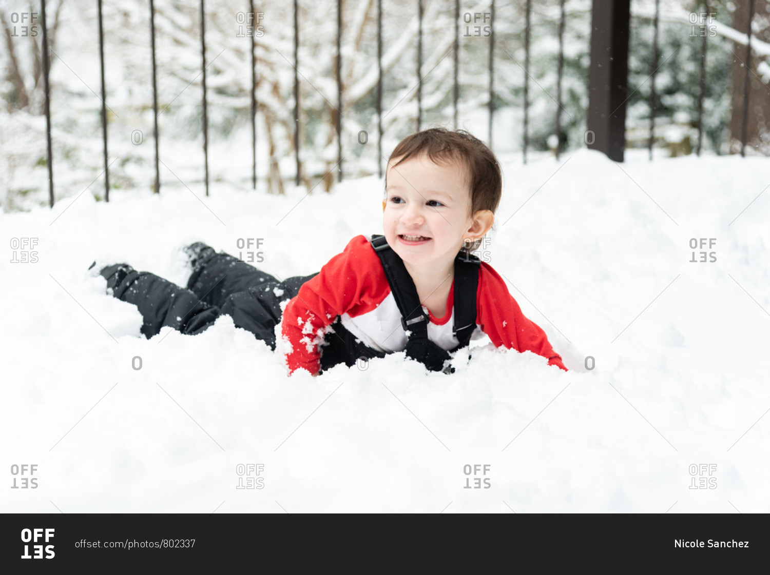 Toddler boy lying in the snow on a snowy deck