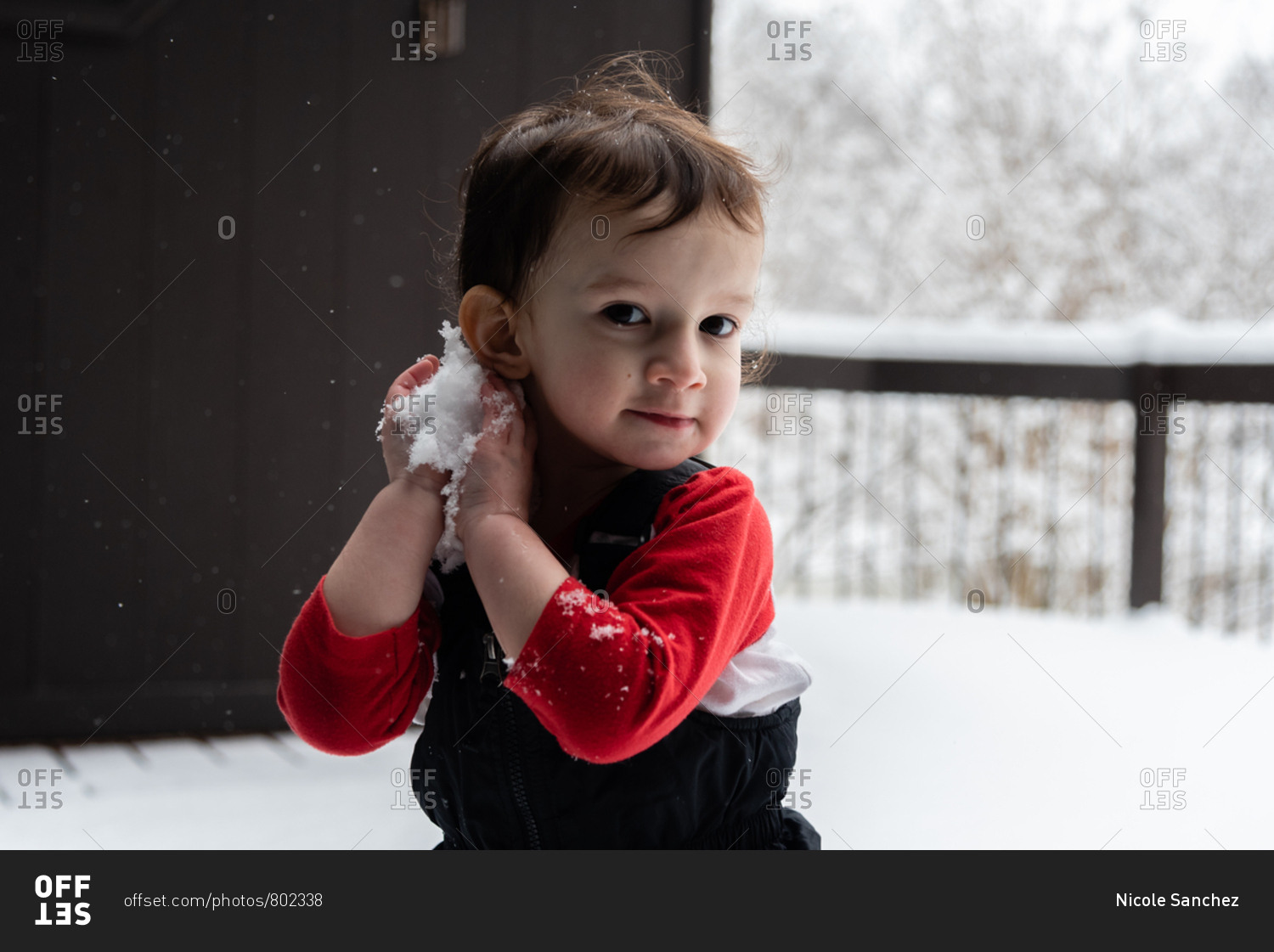 Toddler boy playing with snow on a snowy deck