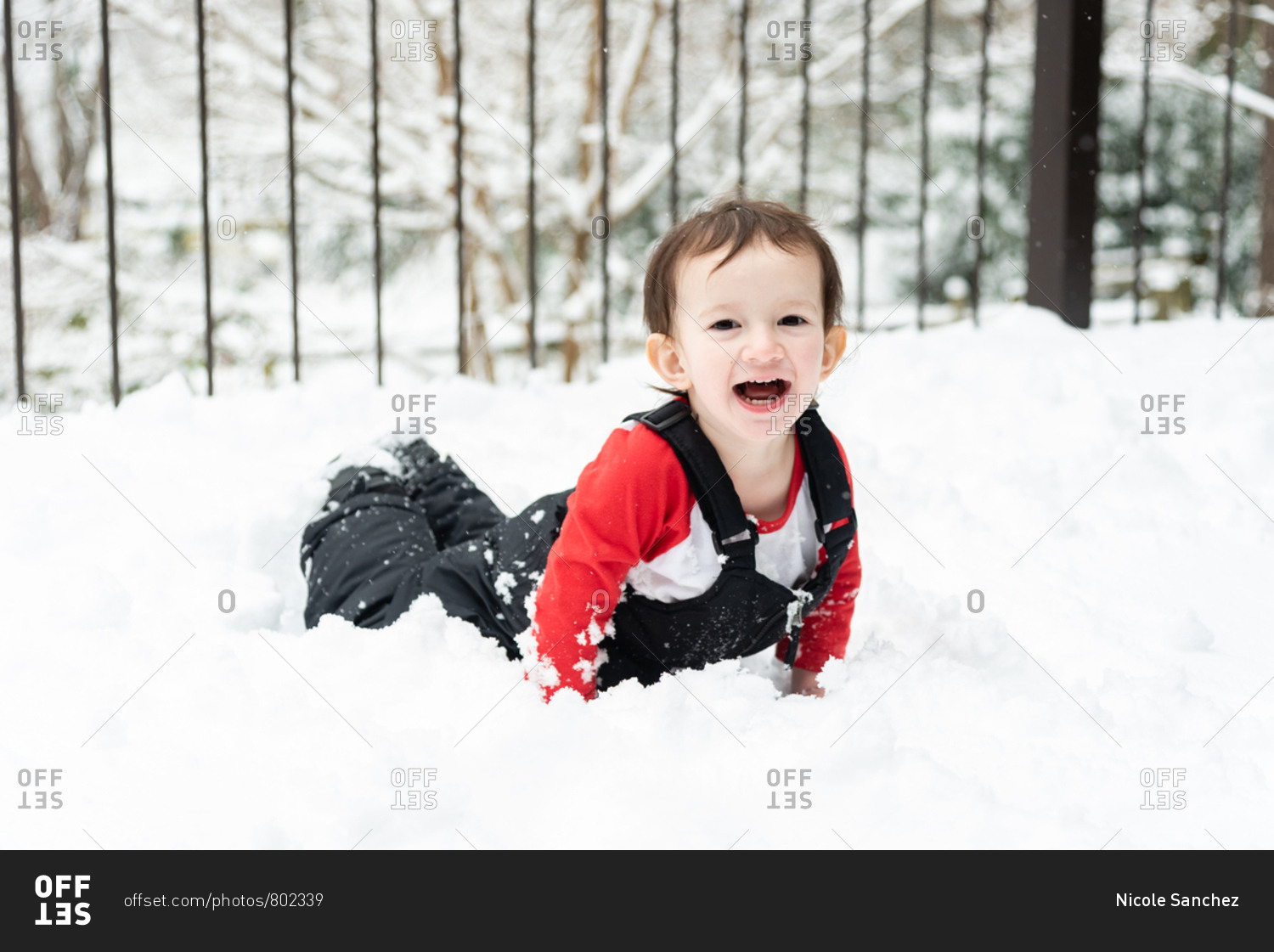 Happy toddler boy playing in the snow on a snowy deck