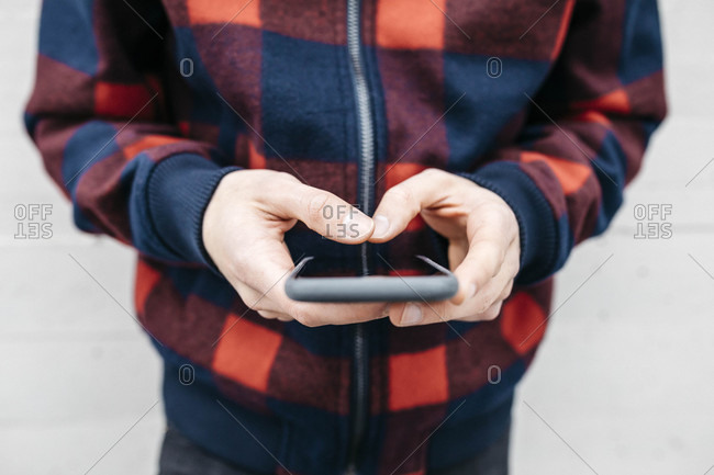 Hands of young man with checkered jacket using phone