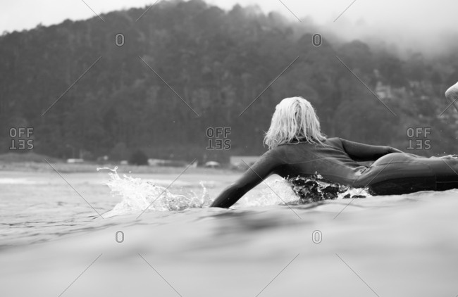 Platinum blonde girl in a wetsuit paddling on her surfboard