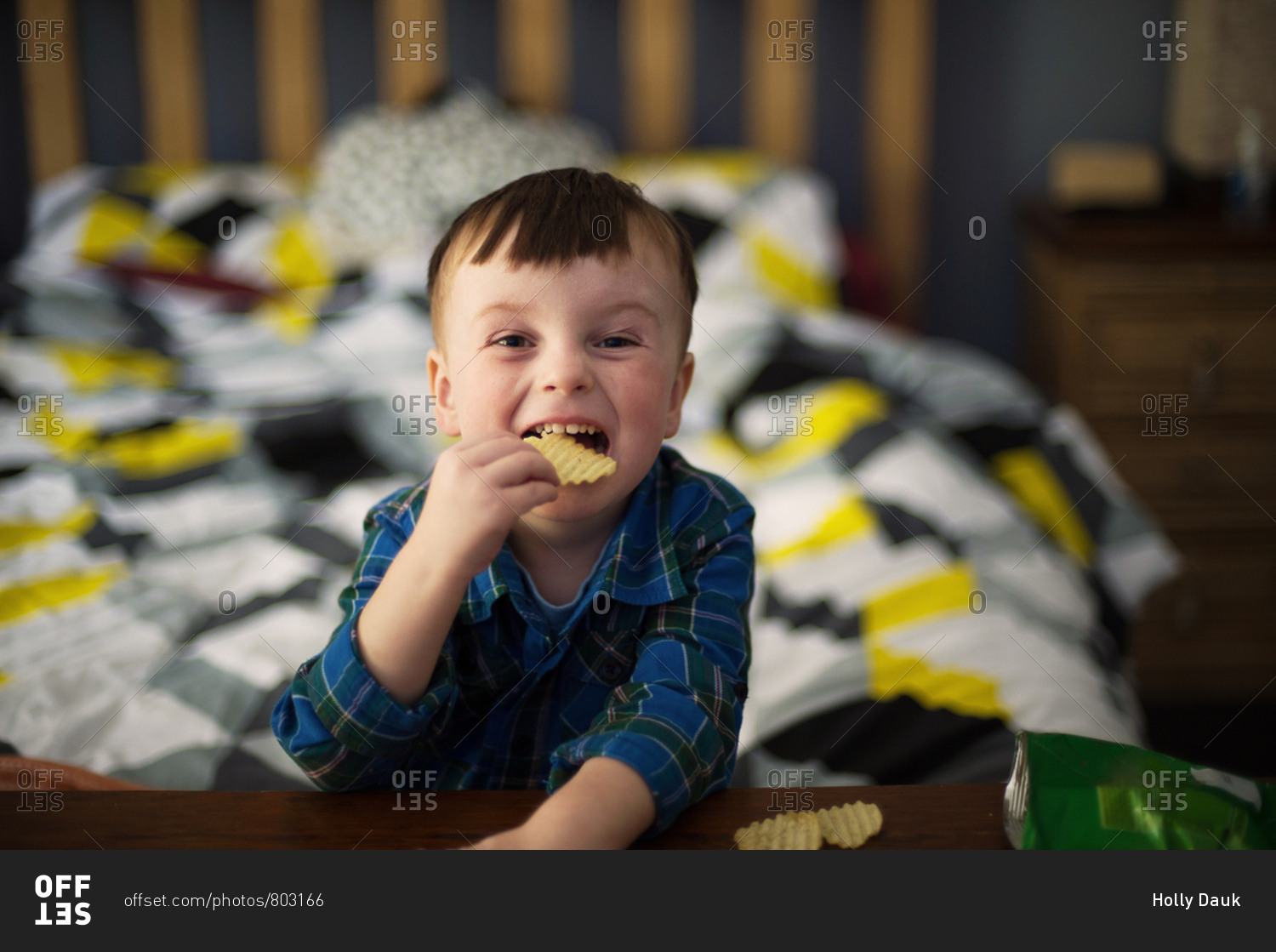 Boy eats a bag of chips in bed