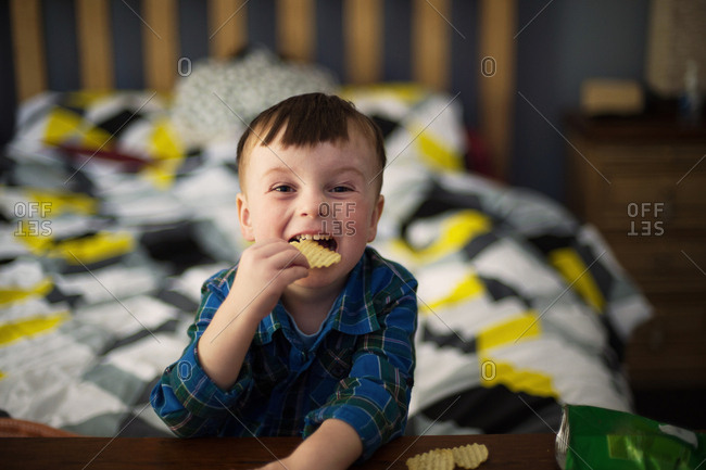 Boy eats a bag of chips in bed