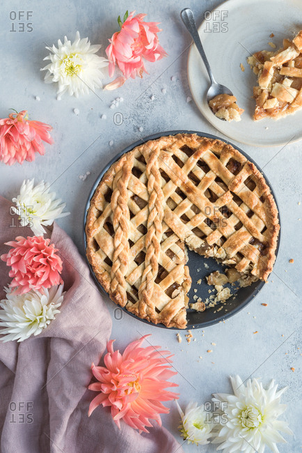Pie in pie-tin with one slice taken out sitting on a plate with a spoon. Accompanied by flowers and a napkin.