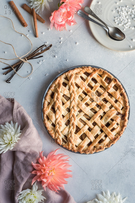 Full fresh pie still in it's tin, set with a plate and spoons near a napkin and flowers.