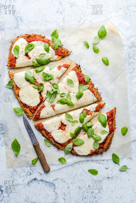 Homemade margherita pizza sliced into pieces with raw basil and a knife.