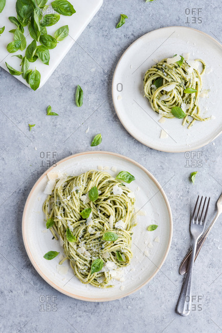A plate of pesto pasta with silverware and a dish of basil.