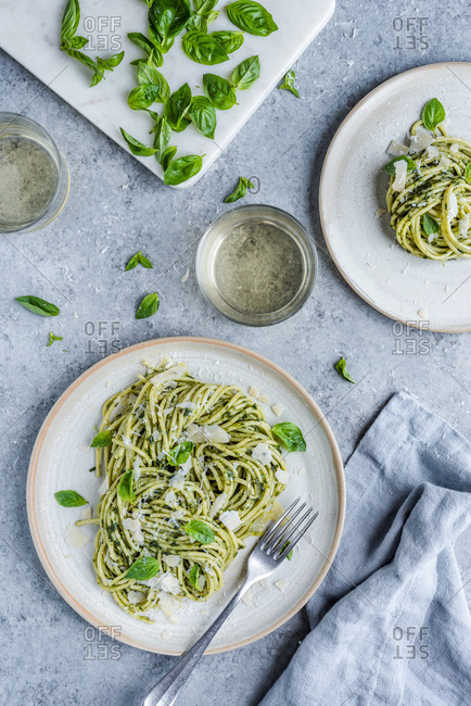 A plate of pesto pasta with a fork accompanied by a drink and a dish of basil.