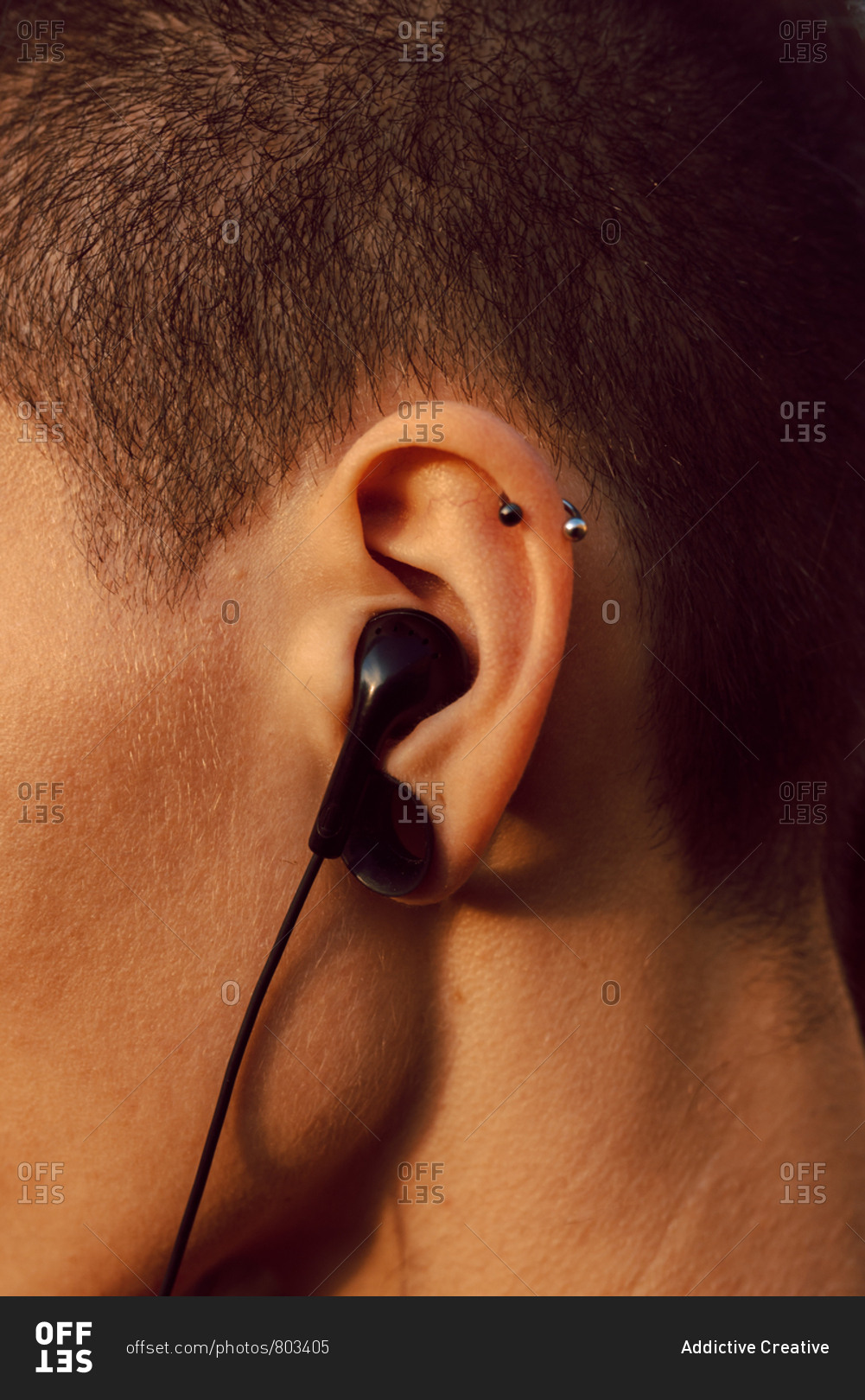 Side view of crop head of hipster with piercing and earphones in ear