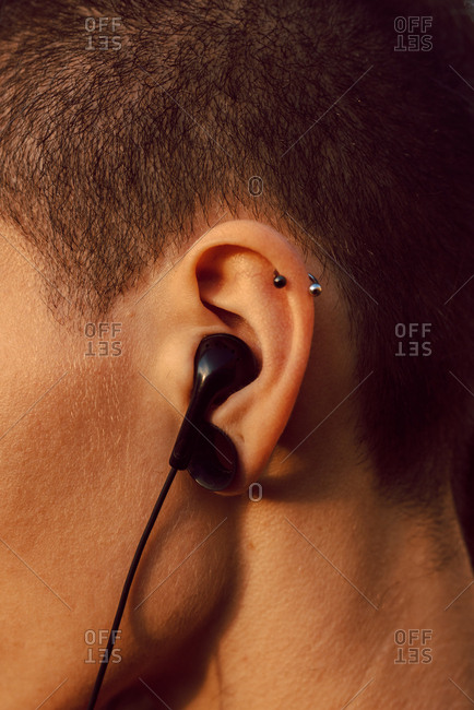 Side view of crop head of hipster with piercing and earphones in ear