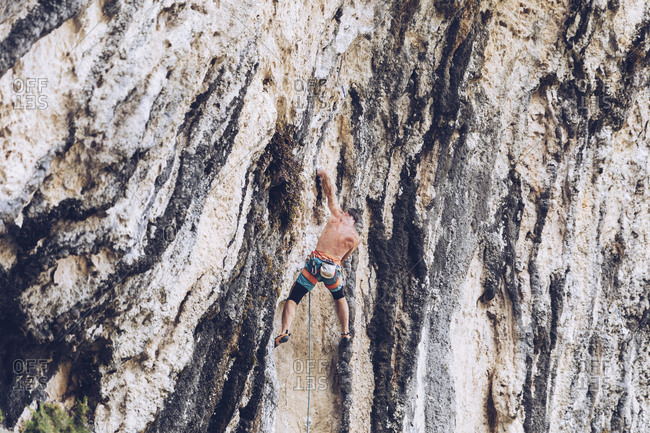 Side view of unrecognizable male in shorts climbing up rough cliff on sunny day in countryside