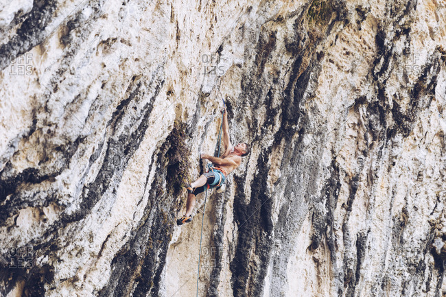Side view of unrecognizable male in shorts climbing up rough cliff on sunny day in countryside