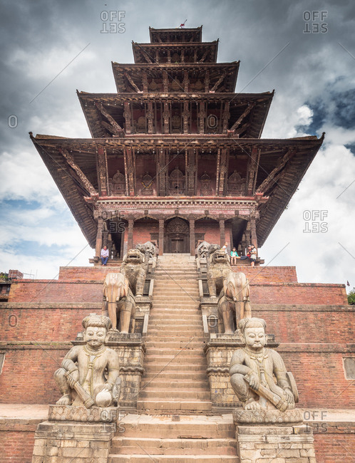 NEPAL, BHAKTAPUR - AUGUST 19, 2014: From below beautiful brick tower with steps and stone monuments and cloudy heaven