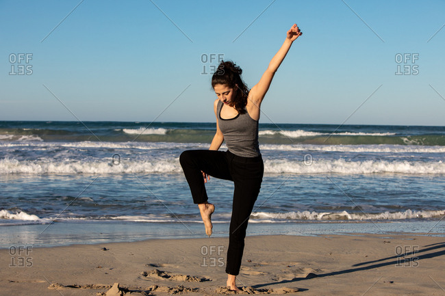 Young dancer on sand coast with waving sea and blue sky