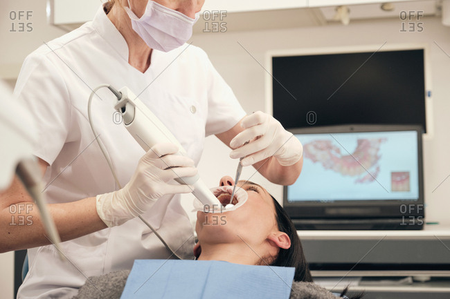 From above woman in gloves and mask using modern equipment to make scan of teeth of female patient in dentist office