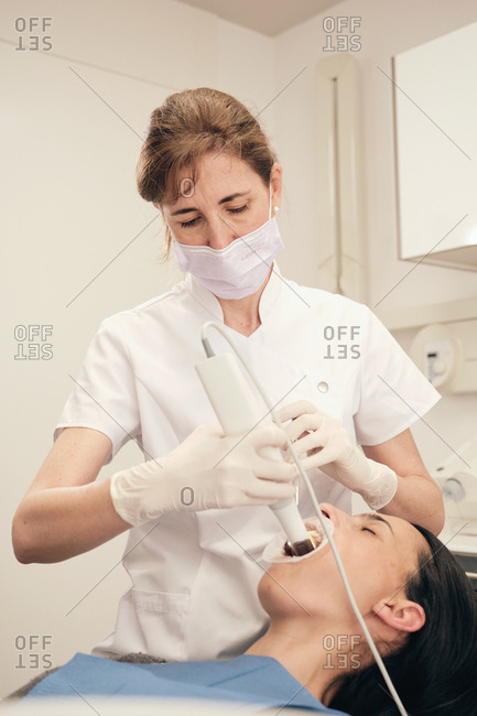 female dentist in gloves and mask using modern equipment to make scan of teeth of female patient in dentist office