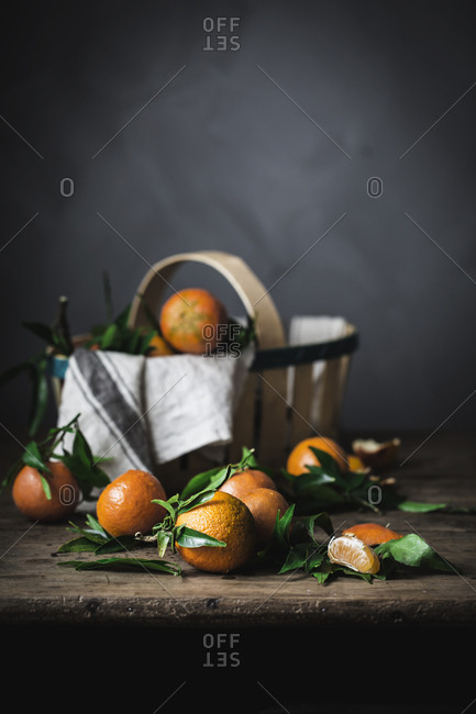 Ripe orange mandarins and basket with towel on rough wooden table