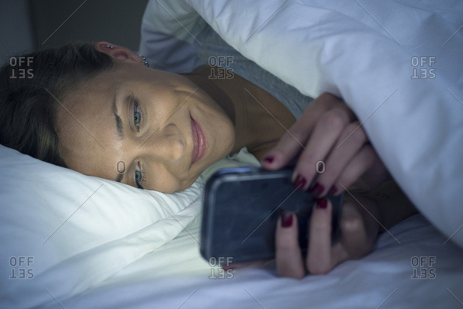 Woman lying in bed using smartphone