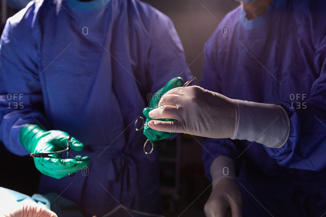 Mid-section of surgeon holding forceps while another holding scissors during surgery in operating room at hospital
