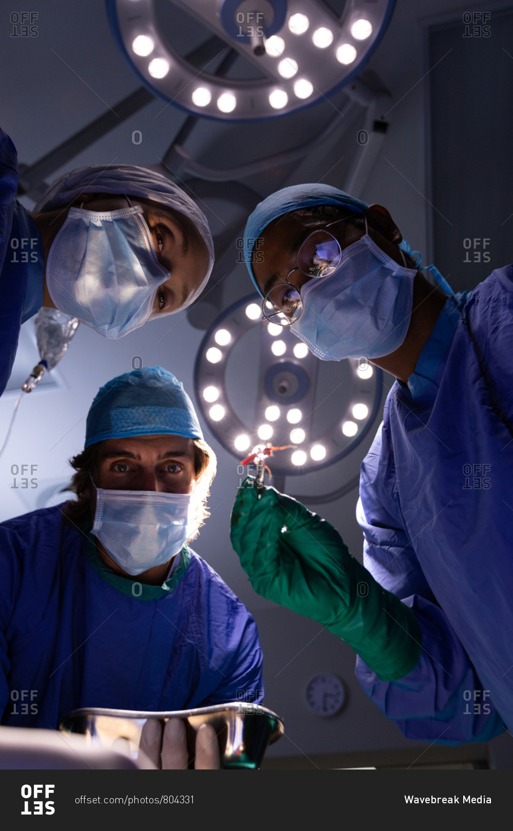 Low angle view of multi-ethnic surgeons concentrated performing operation in operating room at hospital with lights at ceiling