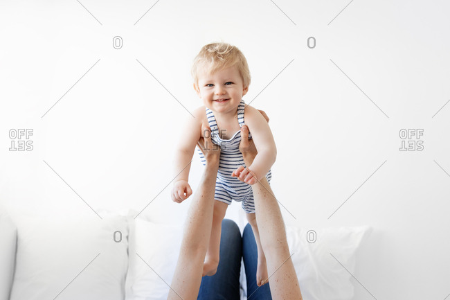 Mother lifting baby with blonde hair and blue eyes in the air