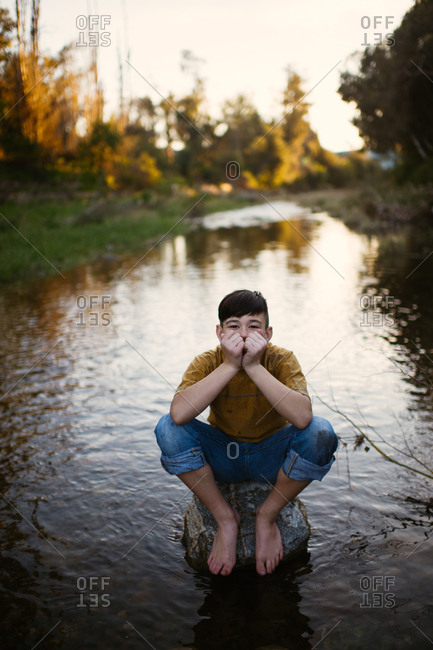 Boy sitting barefoot on rock in a stream