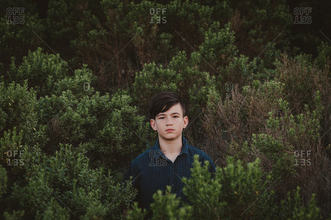 Young teen boy standing surrounded by green plants