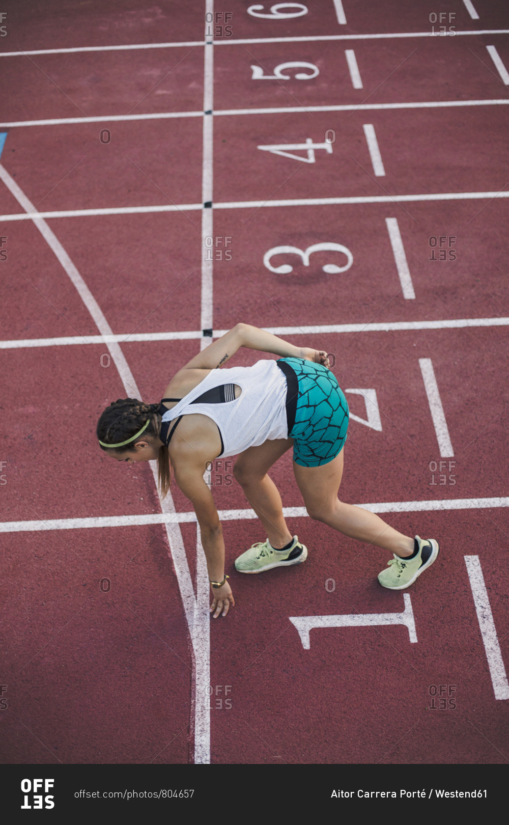 Top view of female runner in starting position on tartan track