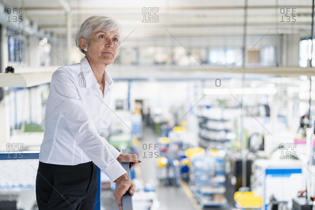 Senior businesswoman on upper floor in factory overlooking shop floor
