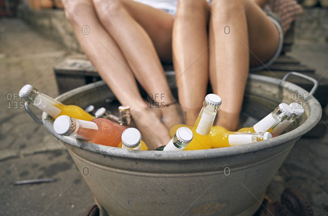 Friends relaxing in a backyard in summer- young women cooling their feet in a tub with drinks