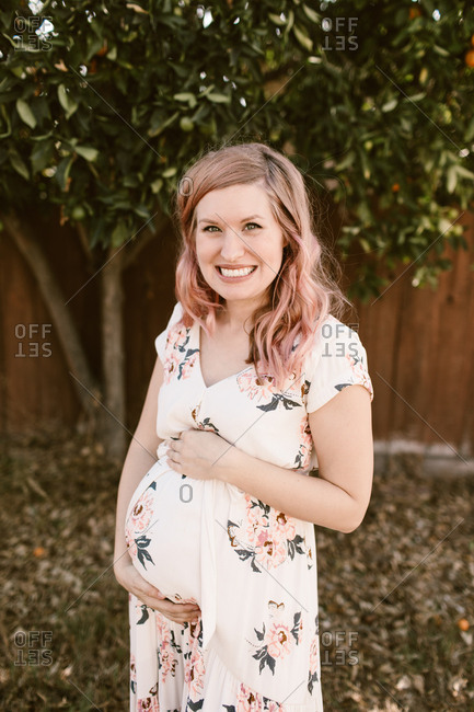 Maternity photo of pregnant woman holding her belly outdoors