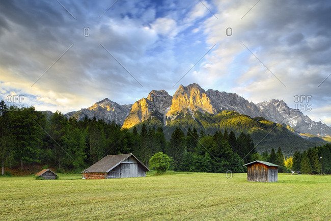 Germany, Bavaria, Bayern, Upper Bavaria, Oberbayern, Garmisch-Partenkirchen, Typical Bavarian landscape with German alps with wooden huts on grass field