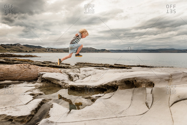 Boy jumping on rock formations by the ocean